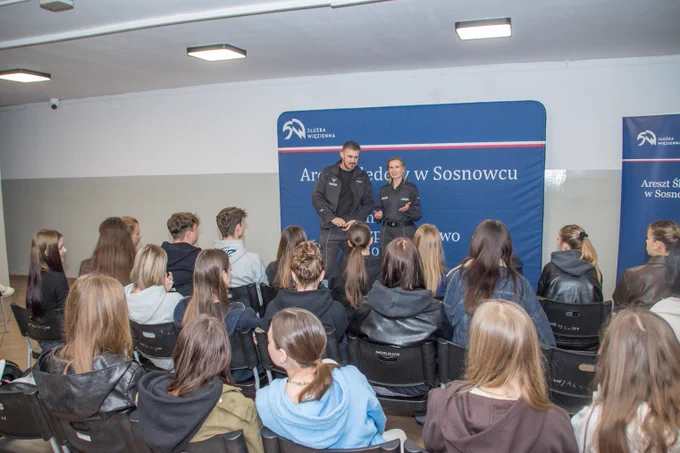 Umundurowani funkcjonariusze stoją przed grupą uczniów.
