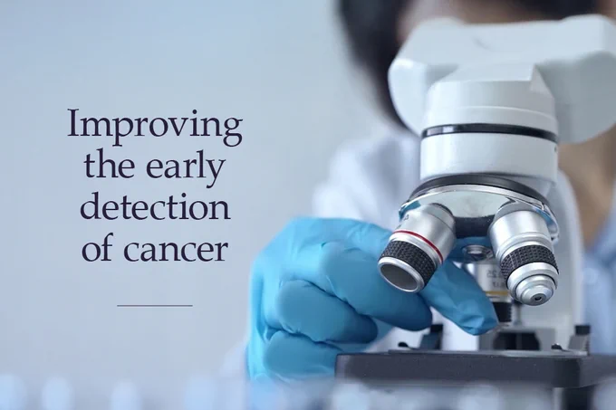A person wearing blue gloves is adjusting a microscope. The text next to the image reads, "Improving the early detection of cancer."