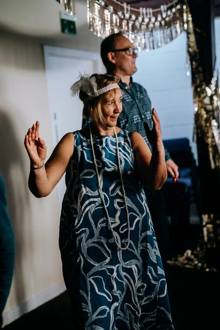 People wearing flapper accessories dance and clap.