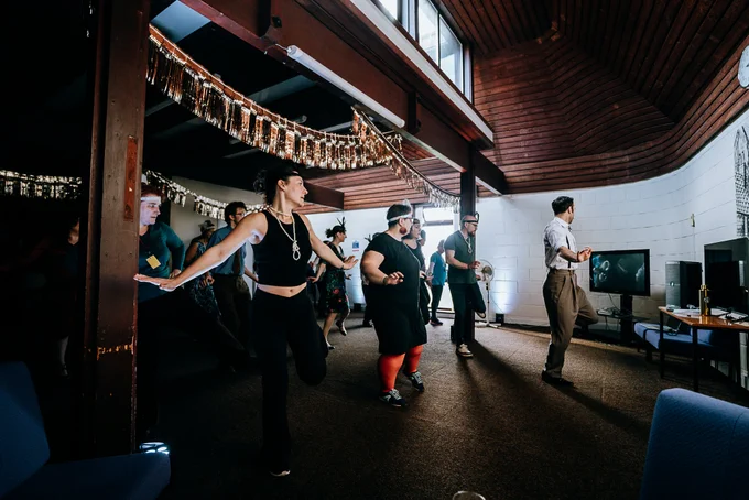 People wearing flapper accessories dance in a small hall.