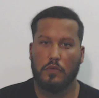 Mugshot of a man with dark hair, beard, and moustache looking directly at the camera.