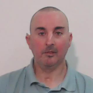 A middle-aged man with a shaved head and red cheeks, wearing a blue polo shirt.