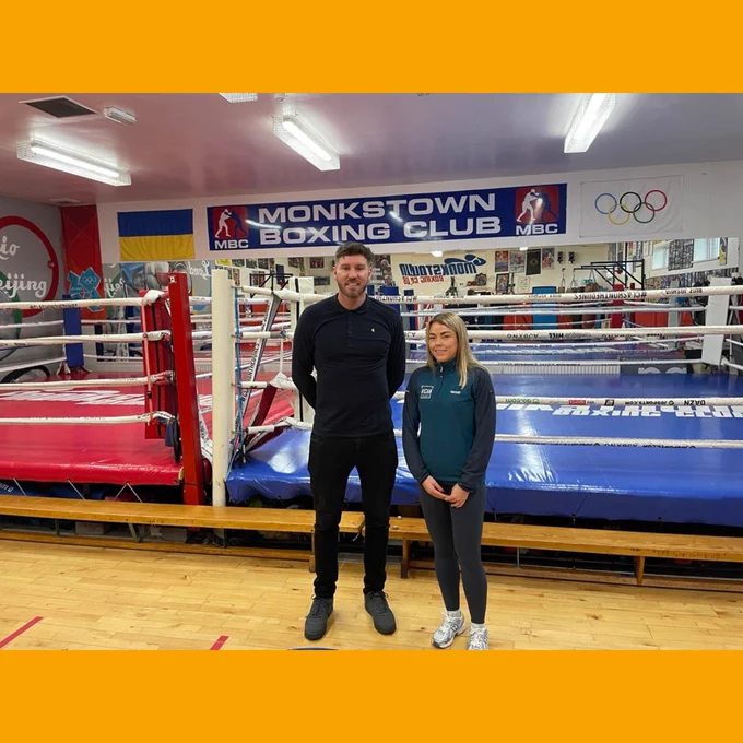 Two people stand in front of red and blue boxing rings