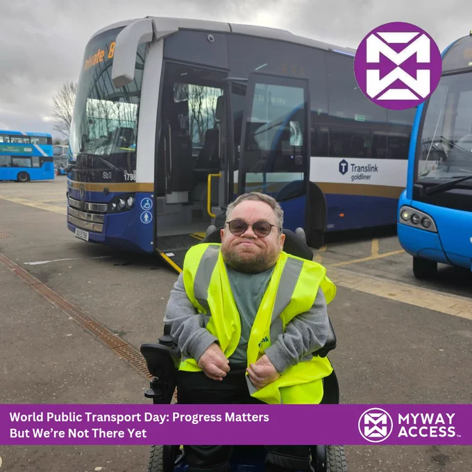 My sitting in my powered wheelchair wearing a yellow safety vest is in front of several buses at a transit station. Text reads: "World Public Transport Day: Progress Matters But We're Not There Yet.