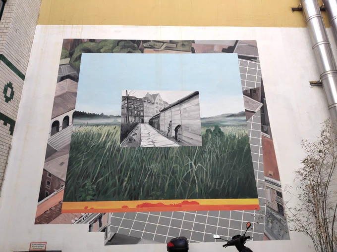 Kunst am Bau: Wand in einem Innenhof mit einem Bild der Berliner Mauer auf einer Wiese.