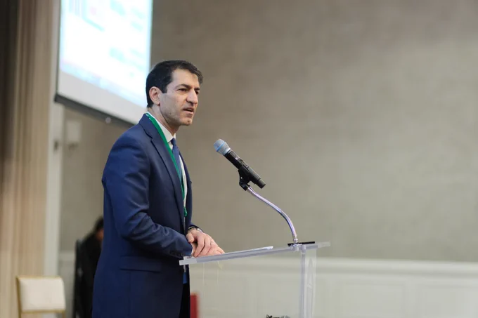 Dr. Nader Jalili stands at the podium and speaks into a microphone, addressing the audience at the Summit. 