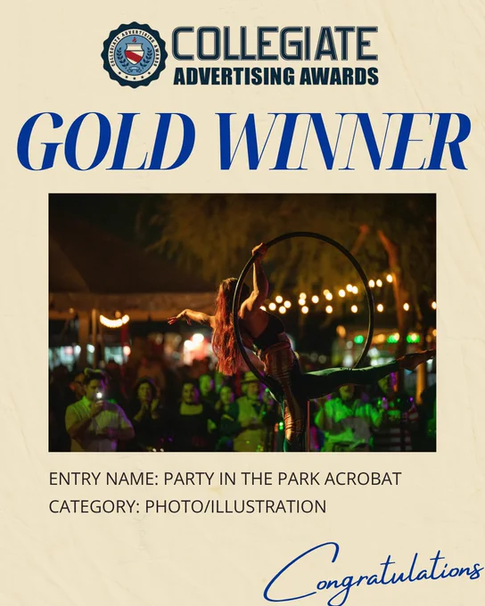 This image shows a "Gold Winner" announcement from the Collegiate Advertising Awards. The winning entry is titled "Party in the Park Acrobat" in the Photo/Illustration category. It features a performer on an aerial hoop with an audience and colorful lights in the background. The word "Congratulations" is written at the bottom.