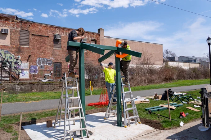 People installing a shade structure along a bike path.