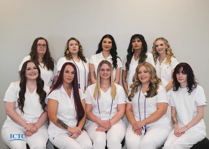Group of women in white uniforms, possibly medical staff, sitting and standing against a white wall.
