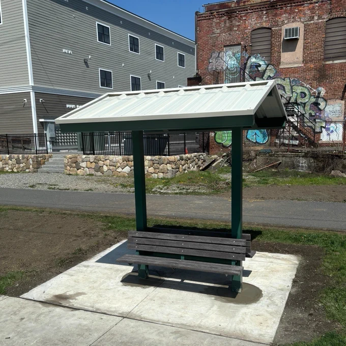 A shade structure over two benches along a bike path.
