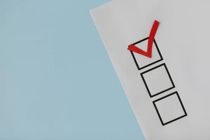 white paper with three black checkboxes, one red check mark through the top box, and a light blue background.