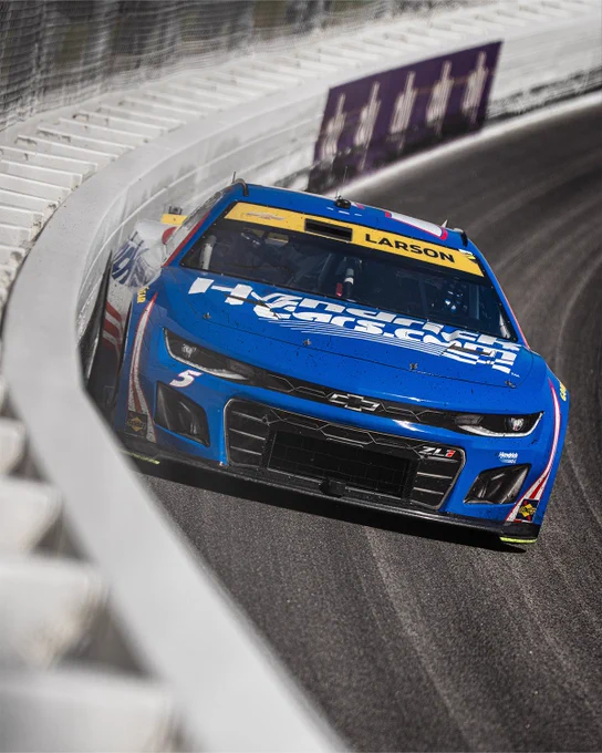 A photo of Kyle Larson racing at Kansas Speedway. He is running inches from the wall. 