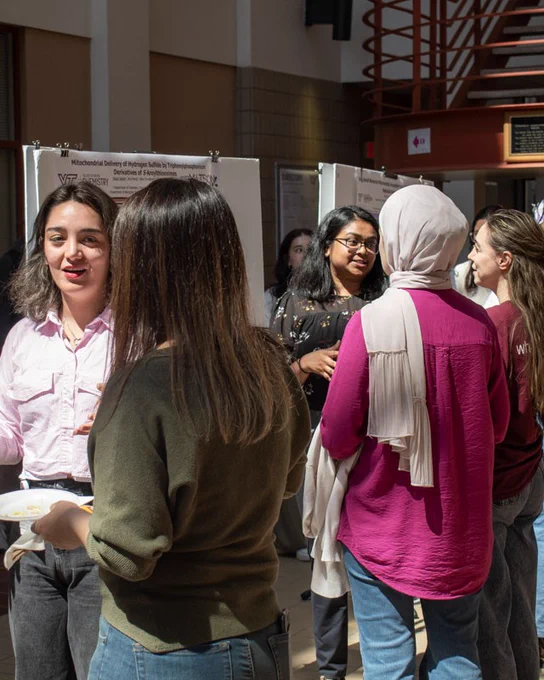 Groups of girls talk with one another in front of their posters. 