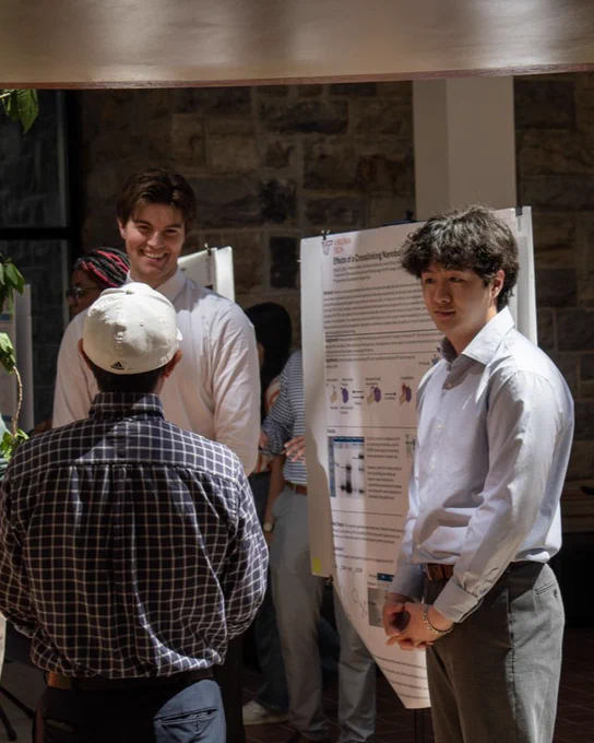 Three guys laugh, smile, and talk with one another in front of posters. 