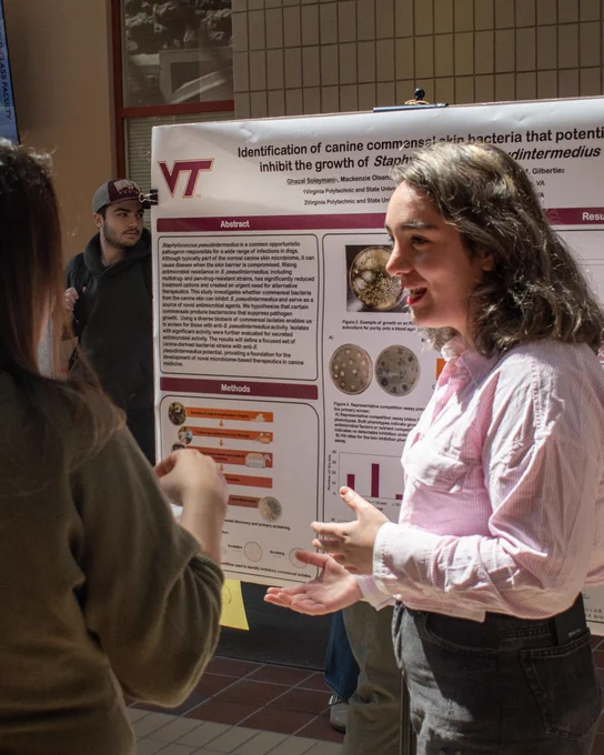 A woman shares her research poster with others. 