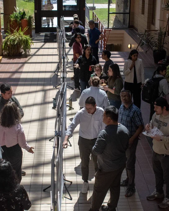 A bird's eye view of the event, showing people walking around and talking with one another about their posters. 