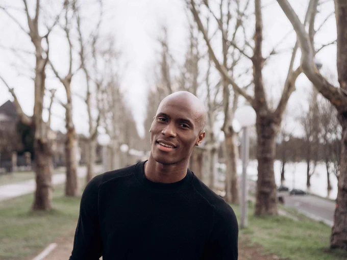 Jamal Callender smiles for the camera in front of a row of trees. 