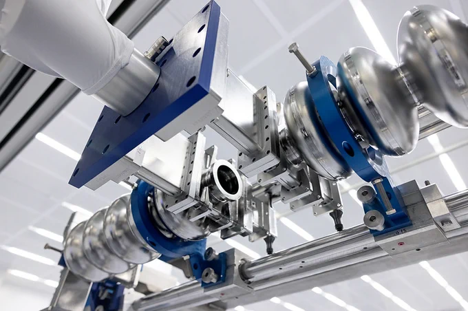 A close-up view of a segment of machinery at Jefferson Lab, featuring metallic components and blue attachments, positioned in a modern, well-lit facility.