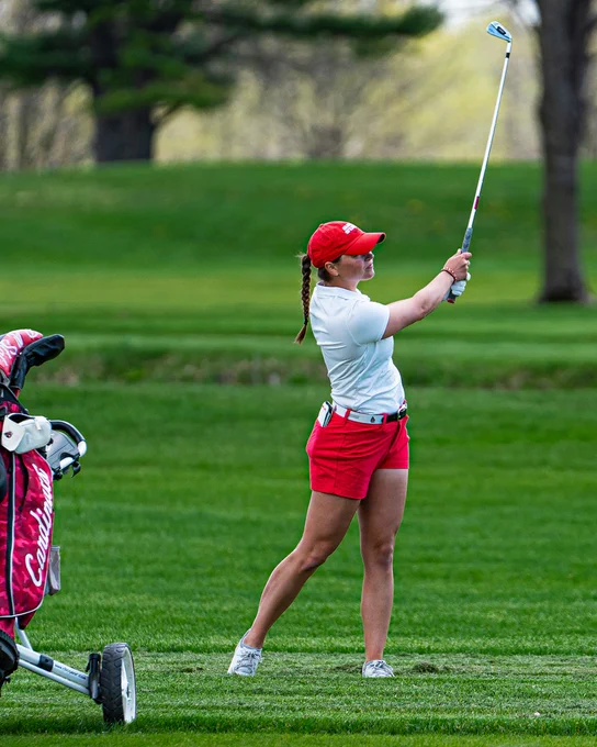 Senior Sabrina Langerak in her red hat, white polo and red shorts hitting an iron shot from the rough during Ball State’s second round at the 2025 Mid-American Conference Championships at the Delaware Country Club in Muncie, Indiana.