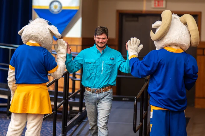 A smiling man walks down a ramp, giving high-fives to two costumed mascots.