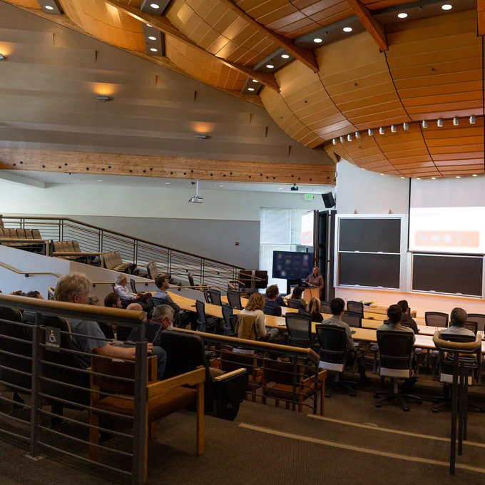The auditorium of the at the Simons Laufer Mathematical Sciences Institute in shades of orange and brown. Dr. Umaa Rebbapragada speaking on machine learning applications  before attendees from the UC Berkeley Space Sciences Laboratory.
