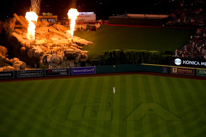 A view from the upper level of Angel Stadium as Mike Trout jogs in the outfield, the large "GA" cut into the centerfield grass in honor of Garret Anderson, while fire is shot upward from the rock pile in celebration of the Angels win. 