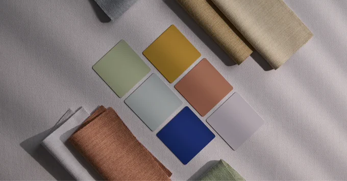 Six rectangular color swatches in muted green, mustard yellow, peach, light blue, navy blue, and pale lavender arranged on a white surface with fabric samples around them.