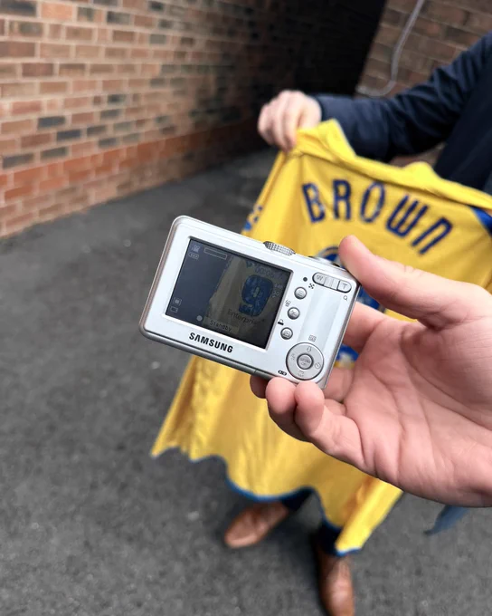 A photo of a Samsung Digimax S500 and an old PNE away shirt with Brown 9 on the back.
