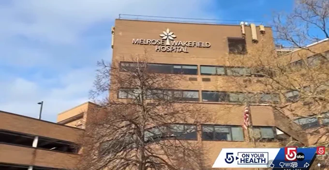 Exterior view of Melrose Wakefield Hospital building under a partly cloudy sky with leafless trees in front.