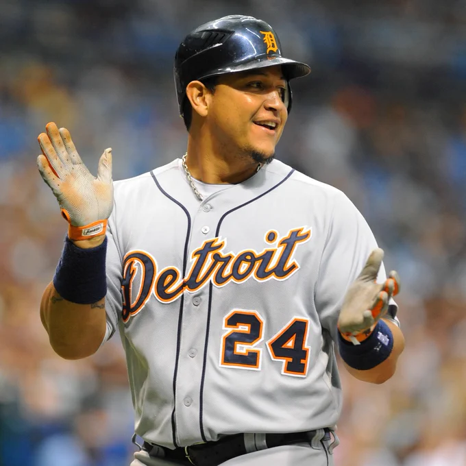 Miguel Cabrera smiles and claps wearing a gray Detroit Tigers uniform with navy lettering and orange trim.
