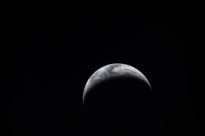 (April 6, 2026) – The Artemis II crew captures an image of a crescent Earth on their journey around the Moon.