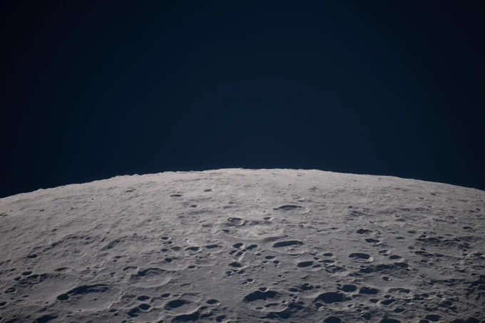(April 6, 2026) – As the Artemis II crew passes the Moon during an observation period, the lunar landscape sharpens into focus: a terrain scattered with craters and shadows stretching beneath the black expanse of space.