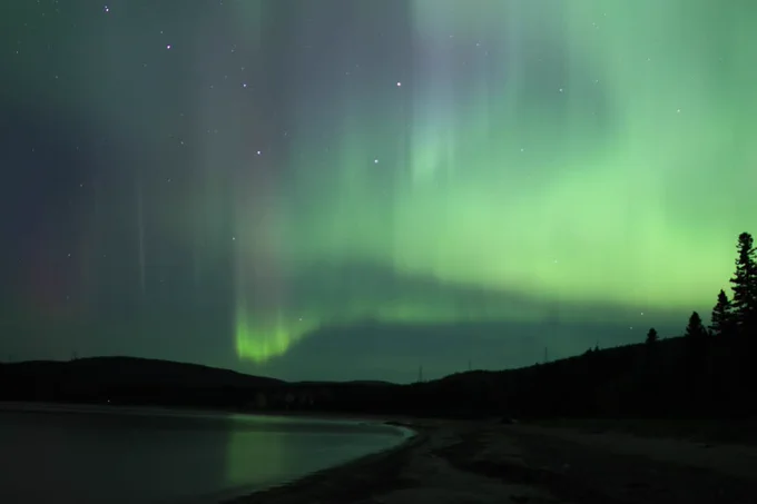 A serene landscape featuring the Northern Lights, or Aurora Borealis, lighting up the night sky with shades of green and purple. 