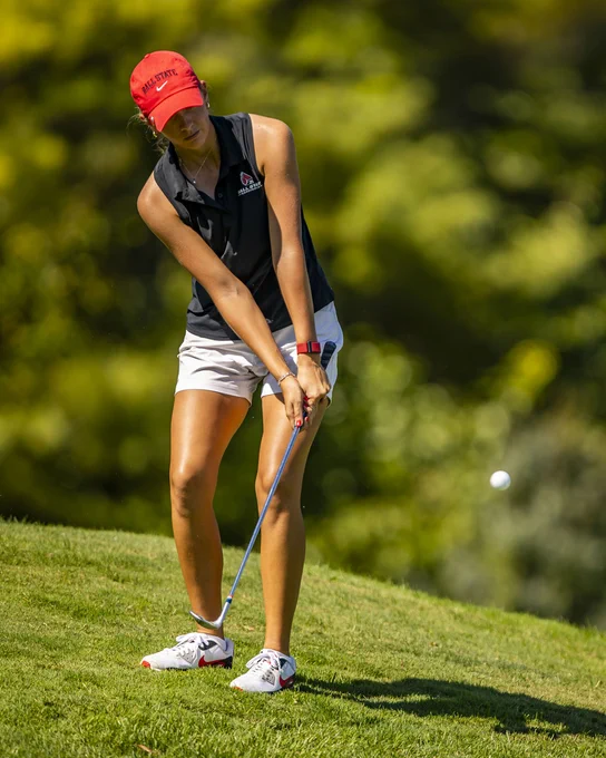 Junior JJ Gregston in her red hat, black polo and white shorts chipping from the rough during the 2025 Brittany Kelly Classic hosted by Ball State at the Players Club at Woodland Trails in Yorktown, Indiana.
