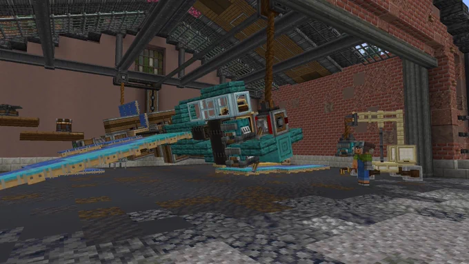 A blue plane made of Minecraft blocks is in a hangar, a wing is detached, and it is being hoisted up by ropes while a player holding tools looks at it.
