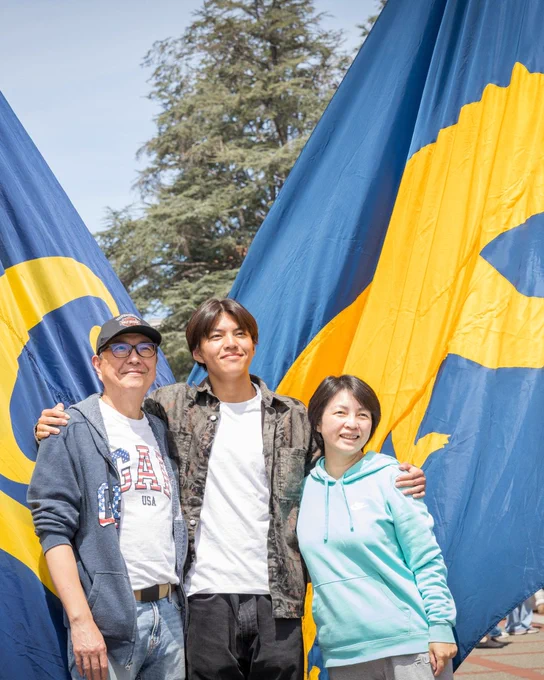 A newly admitted UC Berkeley student posing for a photo with their two guardians in front of blue and gold flags.