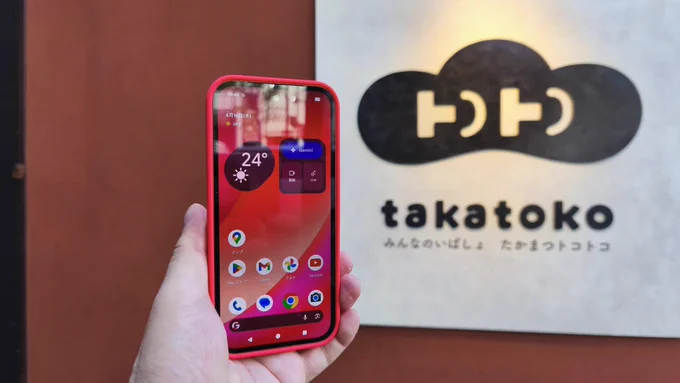 立川のたかまつトコトコ看板前で、補聴器屋の店主が
Google Pixel 10a(赤ケース)を持っている写真。
