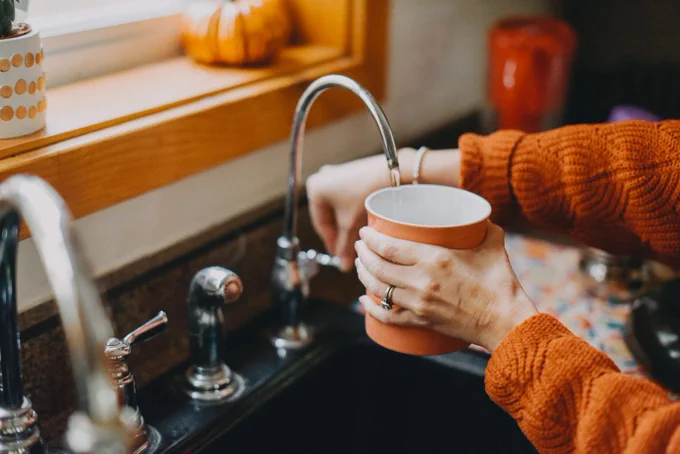 Someone fills an orange mug with water from a kitchen faucet