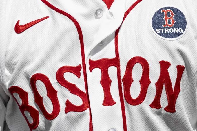 A close up photo of a player wearing the white Red Sox Patriots Day "Boston" jersey with the Boston Strong patch on it.