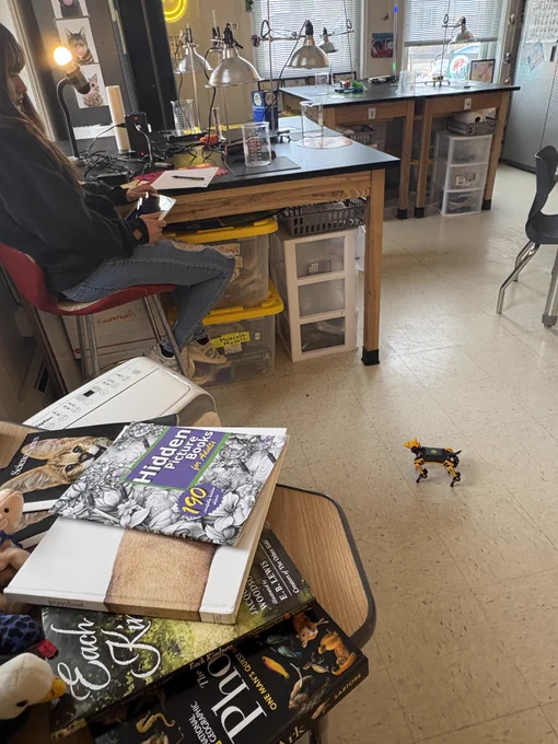 A robot dog stands on the classroom floor, being coded by a student. 