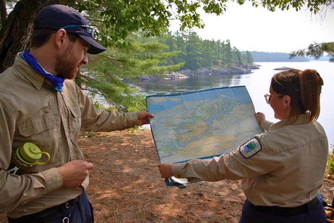 Two Ontario Parks staff members holding open and reading a map on a campsite.