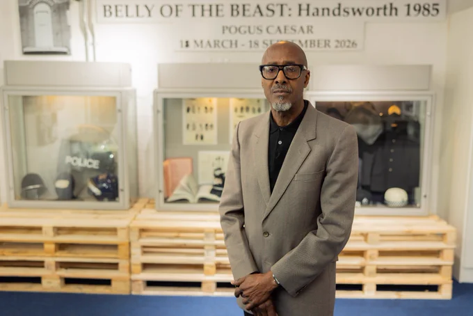 Pogus Caesar can be seen stood in front of display cases which feature items relevant to the exhibition