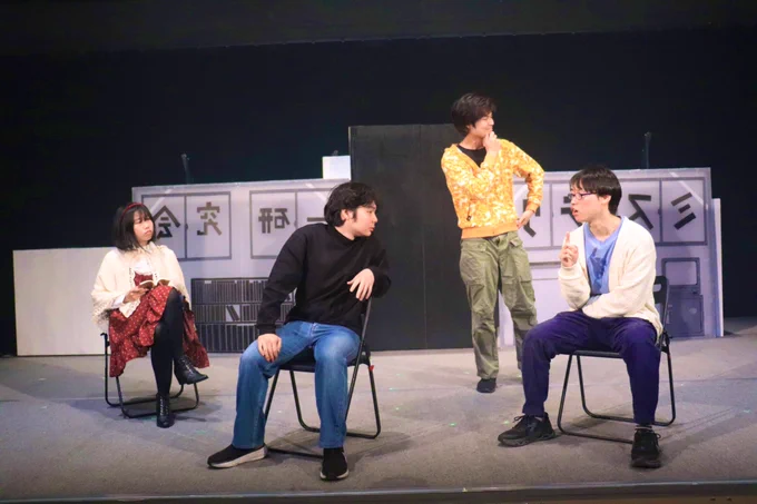 「Phantom Trigger 〜絶対解明〜」の舞台写真

舞台上で4人の人物が集まり話し合っている
舞台下手には赤いワンピースに生成色のポンチョを羽織った人物(いといけいと)、中央には黒い長袖Tシャツにデニムを履いた人物(海老原飛烏)、上手には水色のTシャツにアイボリーのカーディガンを羽織った人物(JT)が椅子に座っている
その後ろにはオレンジ色のパーカーにオリーブグリーンのカーキパンツを履いた人物(楠木涼一)が立っている

舞台奥の壁面には部室を模した切り絵風の装飾が施されており、窓を表現した部分には「ミステリー研究会」と反転した文字で書かれている