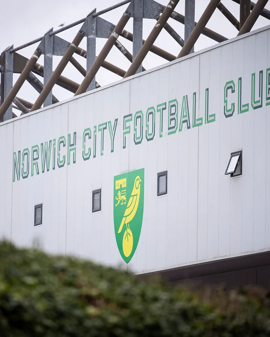 A general image of the exterior of Carrow Road Stadium, including a wall emblazoned with the Norwich City crest and the words "Norwich City Football Club"