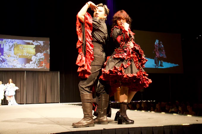 2 people stand back to back on a stage wearing black outfits with red fringe and highlights.