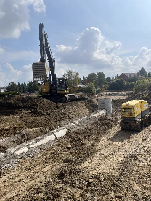 PCL Construction crew installing underground utilities with trenching, pipe placement, and compaction equipment during civil infrastructure work.