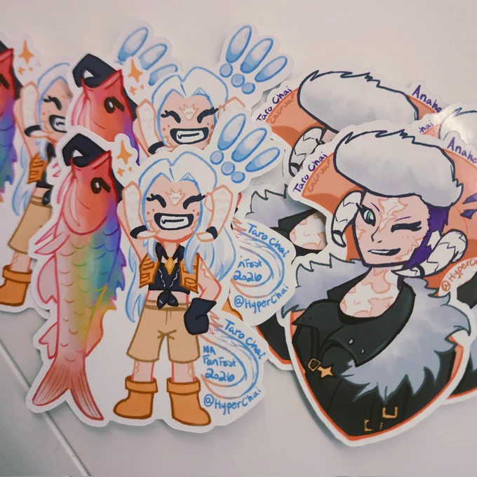 Two versions of stickers of my Warrior of Light, first one is a chibi version of my fem Au Ra holding up the fish Warden of the 7 Hues, a very rainbow fish, and the 2nd is a bust of my WoL winking with a grin in front of the Azem stone.