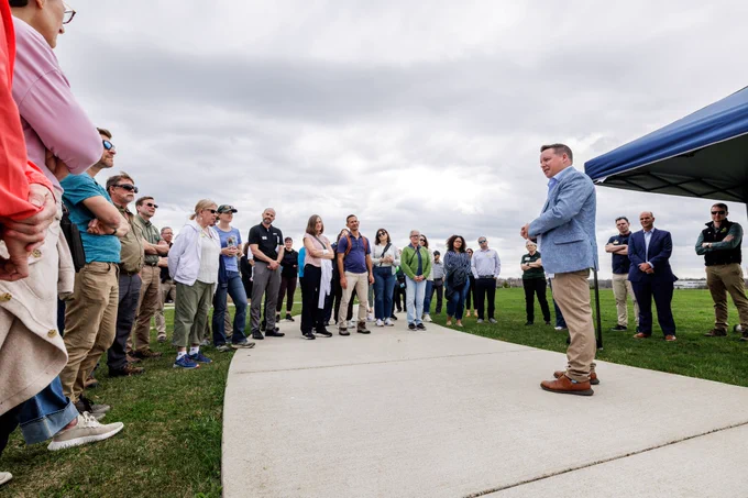 A man addresses a group standing in a semi-circle in an outdoor setting.