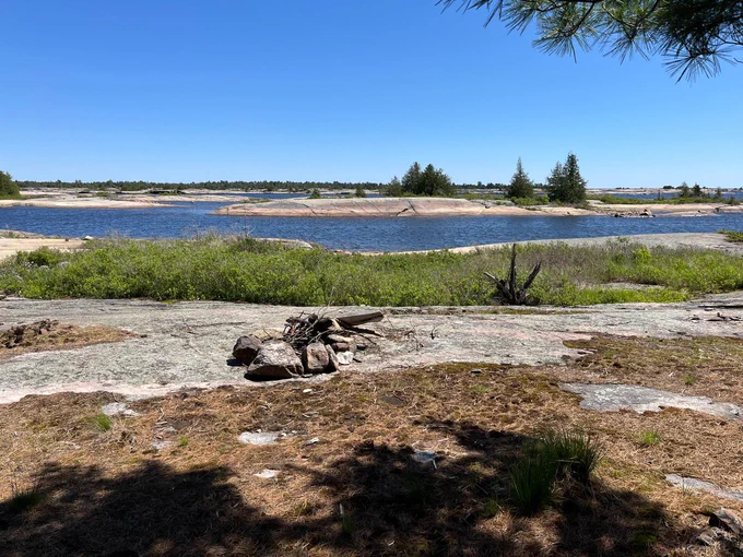 View of a firepit on a rock face looking out towards many rocky islands on a lake.