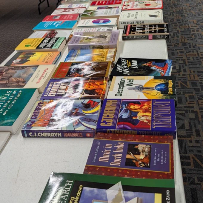 A mix of hardback and paperback books on a white table.